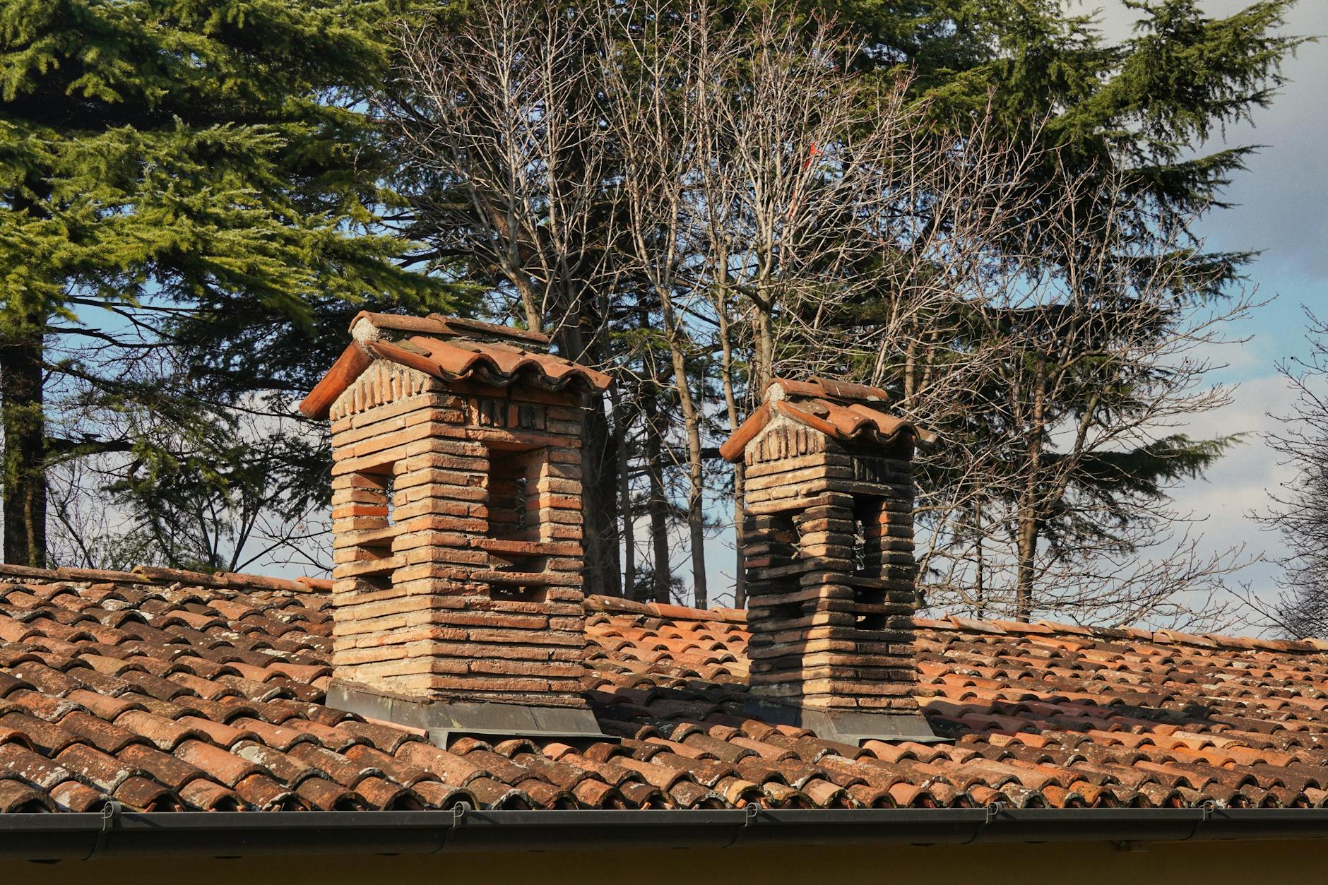 Dwa ceglane kominy na dachu z czerwonej dachówki w zimowym otoczeniu