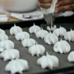 Cukiernik wyciskający waniliowe bezy rękawem cukierniczym na blachę