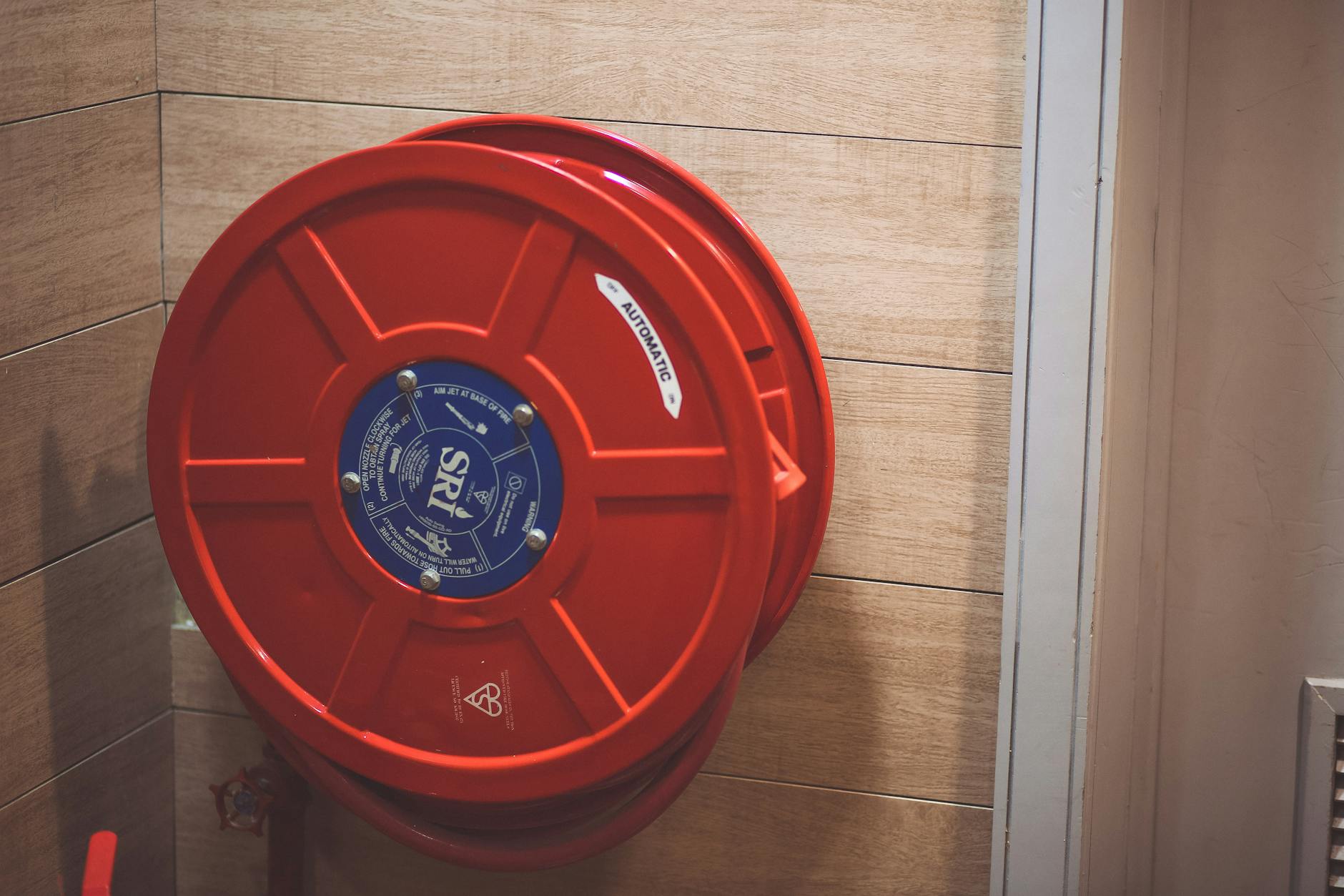 Czerwony bęben z wężem pożarowym na drewnianej ścianie w budynku