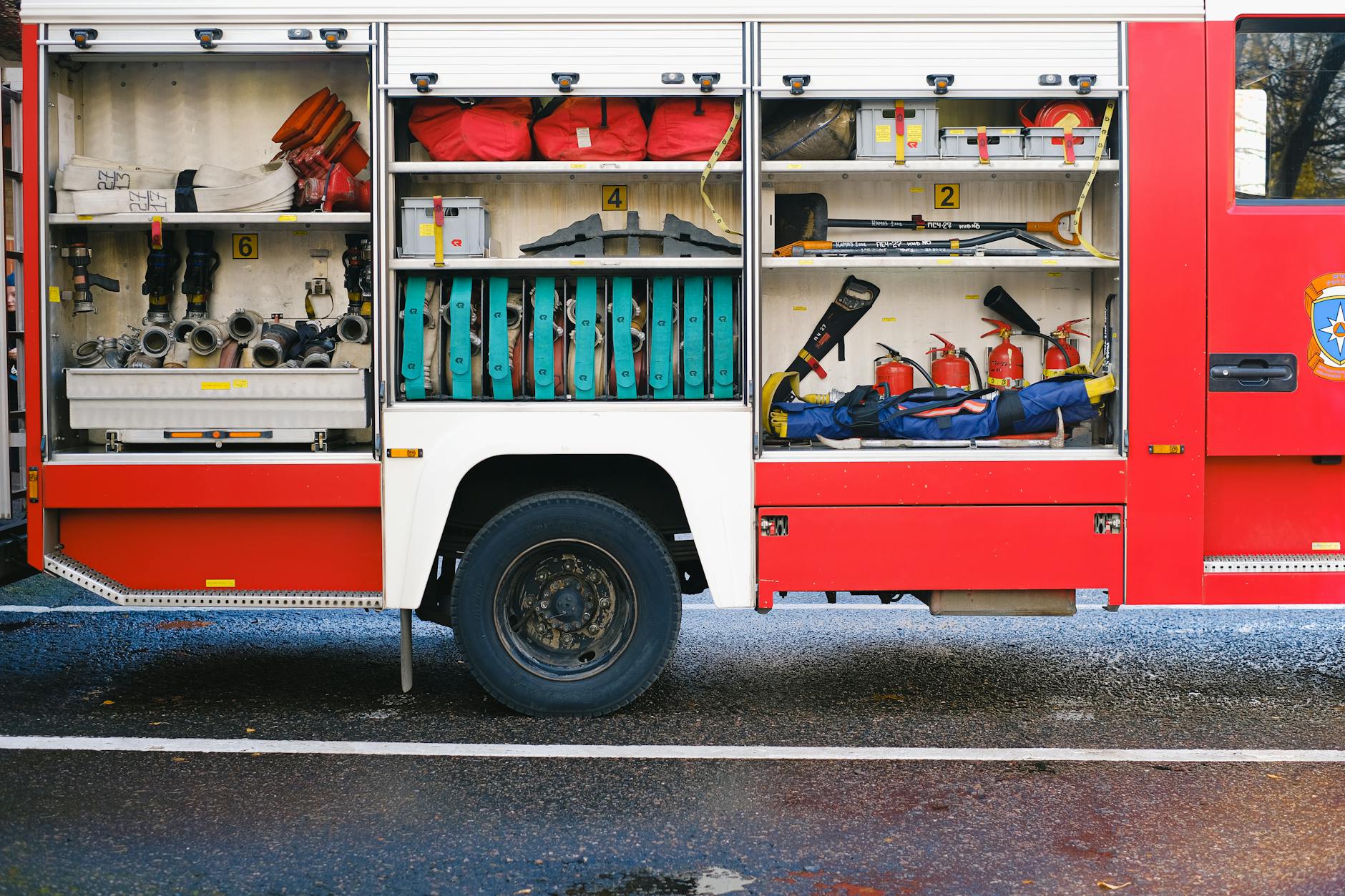 Otwarte schowki wozu strażackiego z widocznym sprzętem gaśniczym