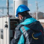 Elektryk w niebieskim kasku sprawdza skrzynkę przy torach kolejowych